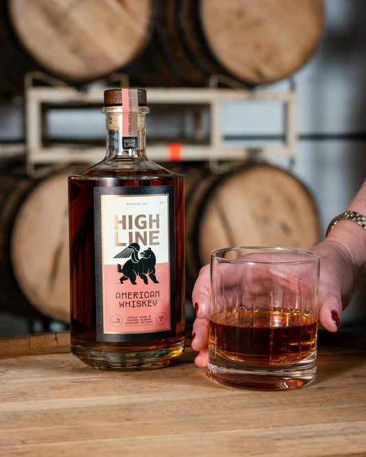High Line American Whiskey bottle and glass with barrels in the background