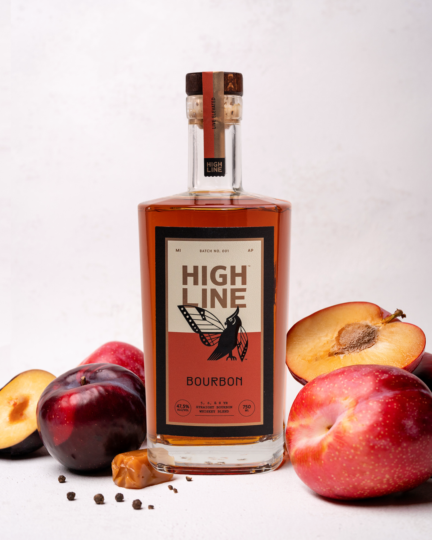 Bottle of High Line Bourbon with plums and a clove on a white background