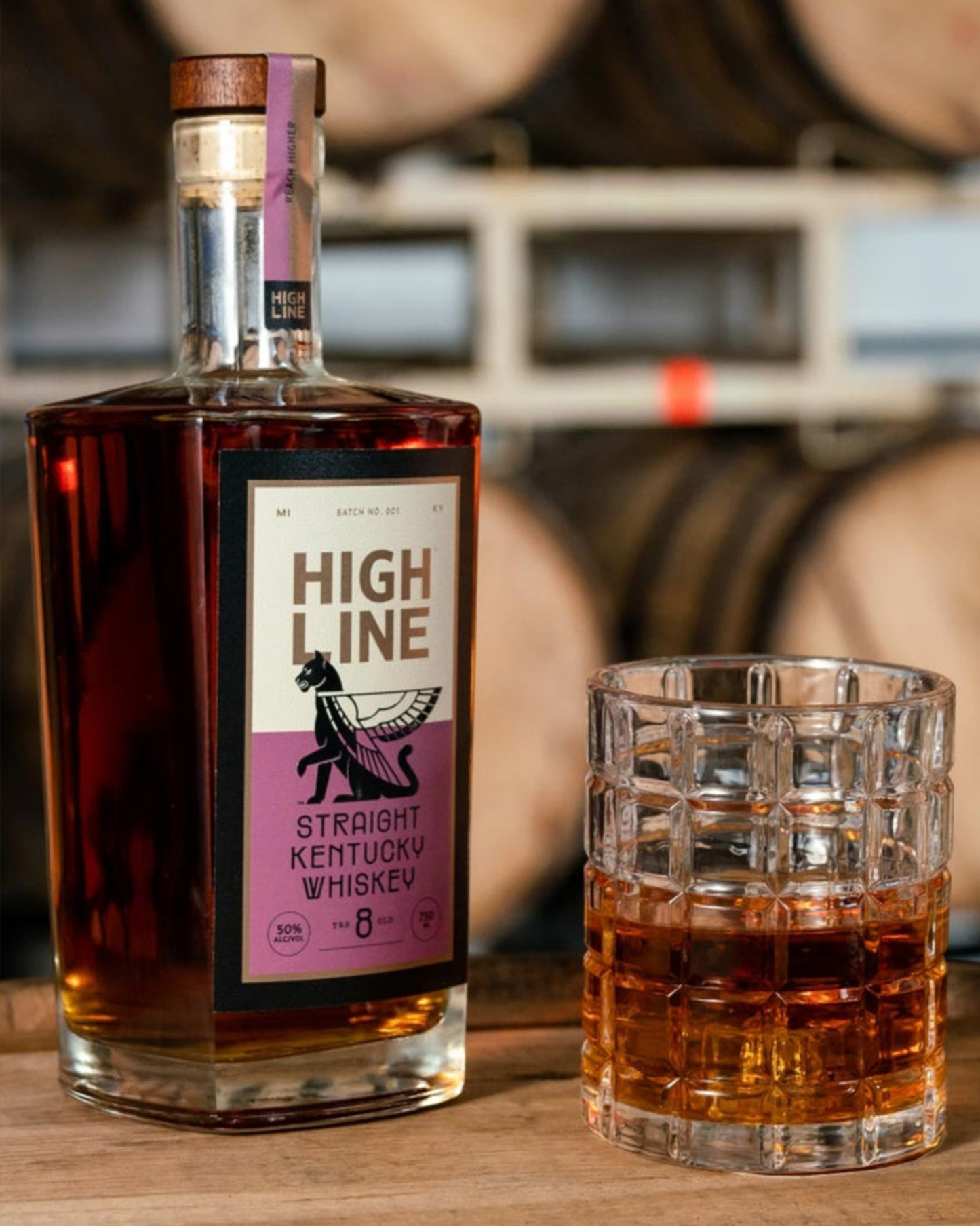 High Line Straight Kentucky Whiskey bottle with a glass of whiskey in front of barrels.