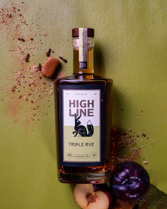 Bottle of High Line Triple Rye on a green background with fruit